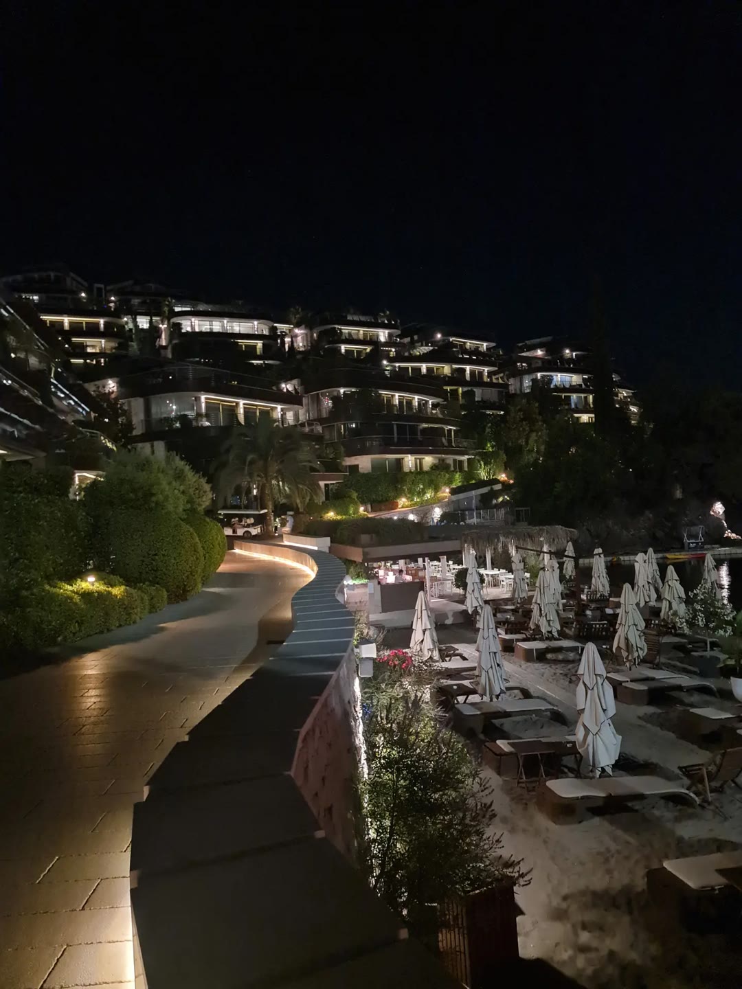 Budva at night: terraced villas lit above the beach and the seafront promenade